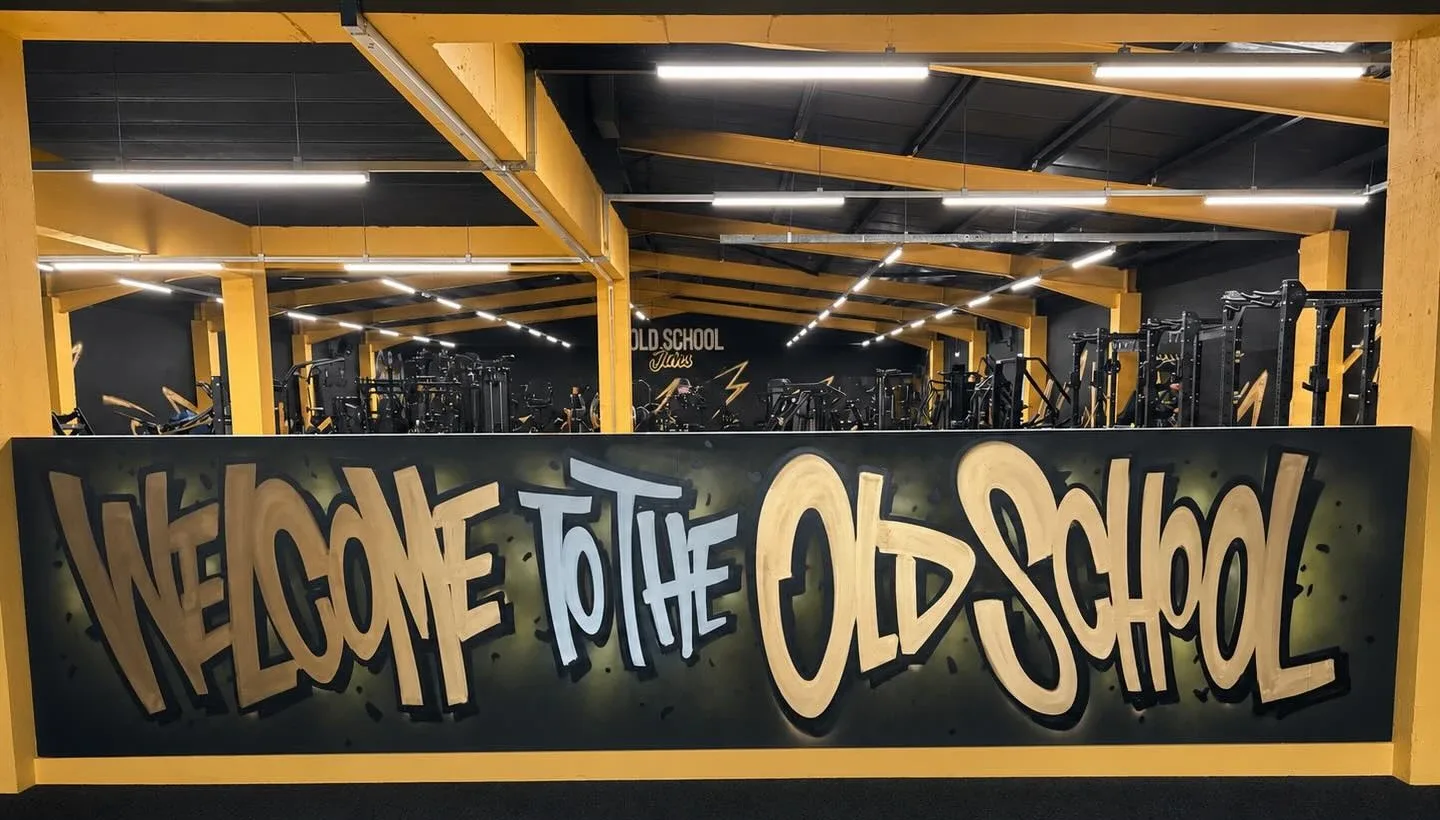 The gym floor behind a hand-painted wall reading Welcome to the Old School, under yellow steel beams